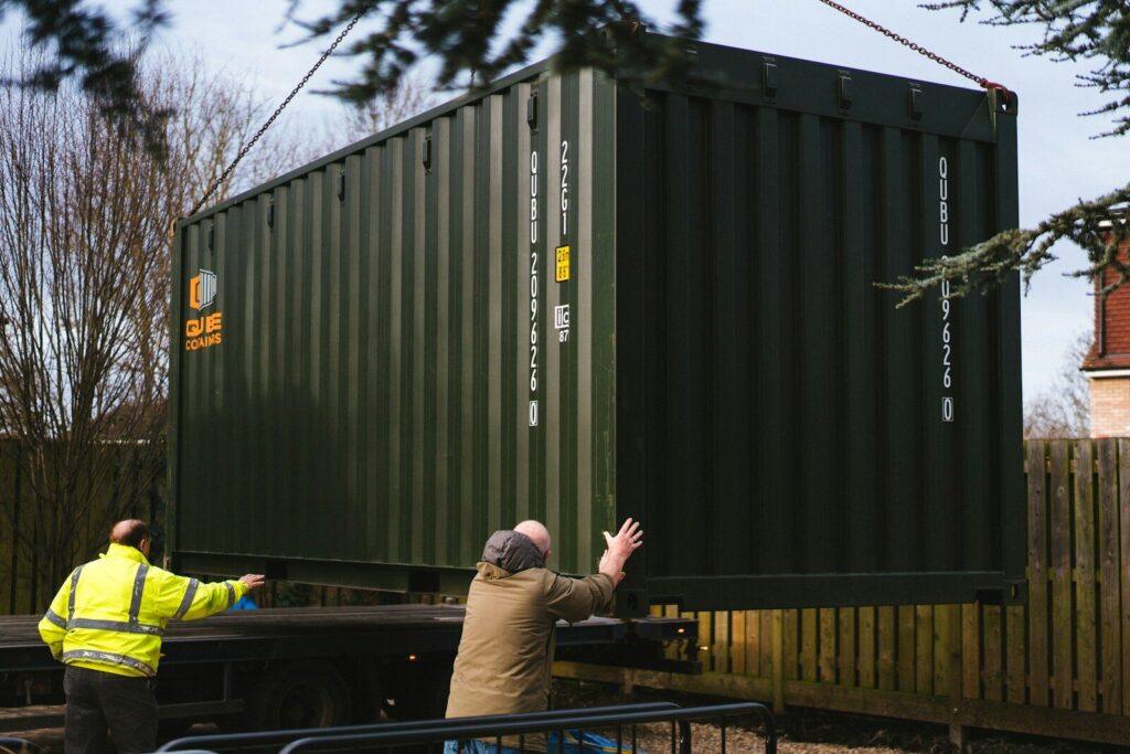 a couple of men standing next to a green container